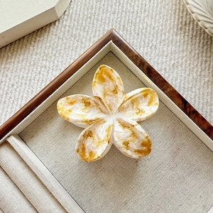 Detailed top view of a marble pattern flower hair claw clip in a beige display box