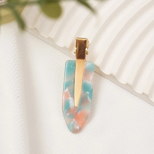 Elegant gold metal hair clip with mint and orange marble acetate design on a wave board