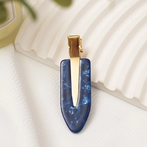 Close-up of blue marble acetate hair clip with golden metal clip on white wave stand