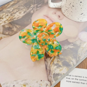 Détail de la pince à cheveux fleur en acétate avec texture marbrée jaune et verte sur magazine