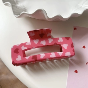 Close-up of a pink acrylic rectangular hair claw clip with heart patterns and rose details