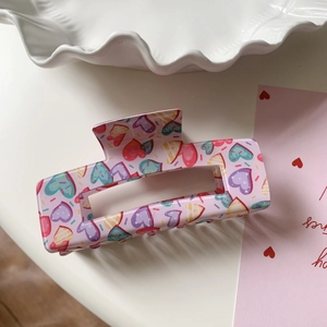 Detailed close-up of pink rectangular claw clip with colorful heart patterns on a ceramic tray