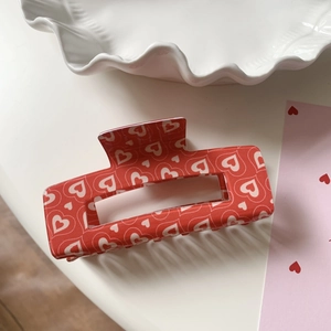 Detail view of a rectangular red acrylic hair claw clip with white heart patterns
