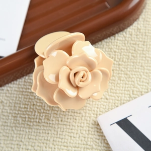 Gros plan d'une pince à cheveux camélia beige en acétate sur un plateau texturé