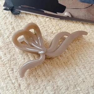 Grande pince à cheveux nude en forme de nœud sur un fond beige texturé