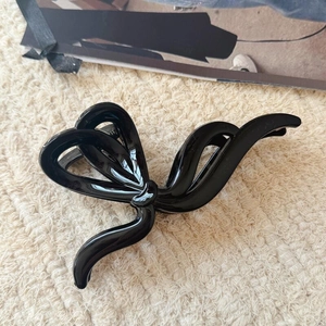 Gros plan d'une grande pince à cheveux nœud noir brillant sur un tapis beige texturé