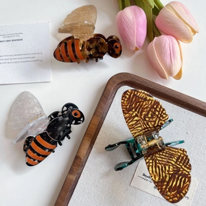 Pinces à cheveux en acétate motif abeille et papillon sur un bureau blanc avec des fleurs