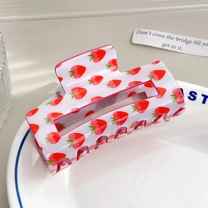 Detailed close-up of strawberry print acrylic hair claw clip on a decorative plate