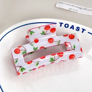 Close-up of a white rectangular hair claw clip with red cherry and green leaf patterns