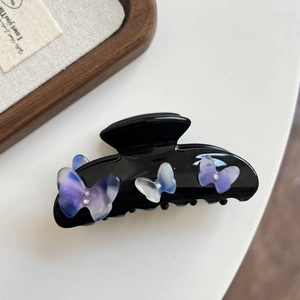 Macro shot of black acetate claw clip with iridescent purple rhinestone butterfly details