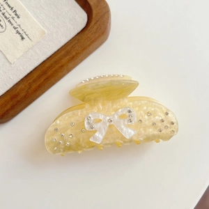 Detail of a pale yellow acetate hair claw clip with marble texture and rhinestone bow