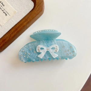 Close-up of light blue acetate hair claw clip with bow design and sparkling rhinestones