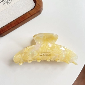 Close-up of cream yellow marble pattern acetate hair claw clip with gold Barrette text