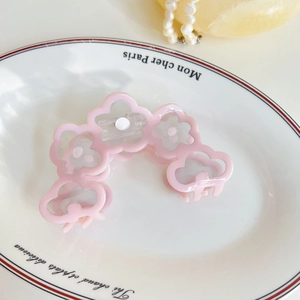 Détail d'une pince à cheveux fleur rose en acétate posée sur une assiette en porcelaine blanche