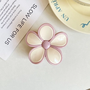 Detailed top view of pink and white frangipani flower hair claw on a ceramic plate