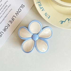 Detailed view of the blue and cream frangipani flower hair claw clip on a book