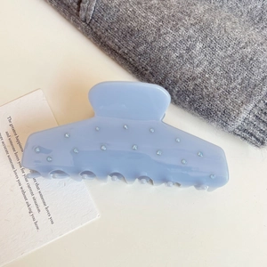Detail view of light blue acetate shark hair claw clip with pearl accents on a white surface
