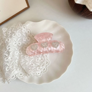 Close-up of a pink acetate hair claw clip with three rhinestone heart decorations