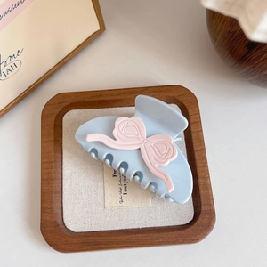 Close-up of pastel blue acetate claw clip with pink bow on a rustic wooden tray