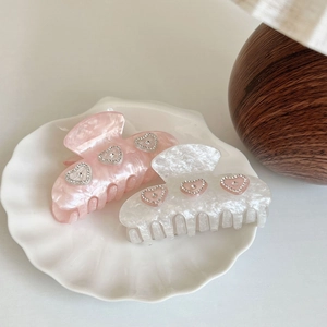 Pink and white acetate heart hair claws with rhinestones in a decorative shell dish