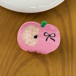 Pink apple-shaped hair claw clip with green leaf and bow pattern on wooden desk