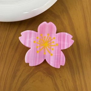 Pink acetate cherry blossom hair claw clip with yellow stamens on a wooden table