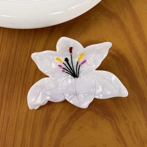 Elegant white lily acetate hair claw clip with floral pattern on dark wood background