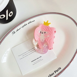 Detail view of a pink mermaid-shaped hair claw clip with a yellow crown on a white plate