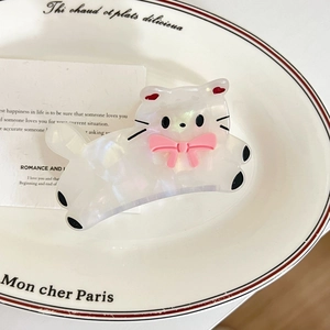 Gros plan d'une pince à cheveux chat en acétate blanc avec nœud rose sur un plat en céramique