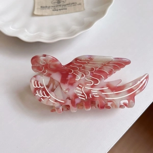 Macro detail of bird-shaped acetate hair claw clip with elegant marble pink patterns