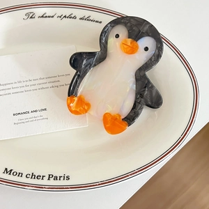 Détail d'une pince à cheveux en acétate en forme de manchot sur une assiette décorative