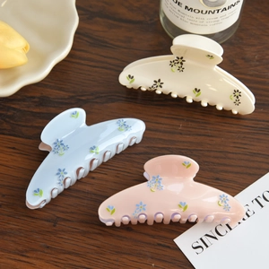Close-up of floral acetate hair claws in blue, cream, and pink on a wood surface