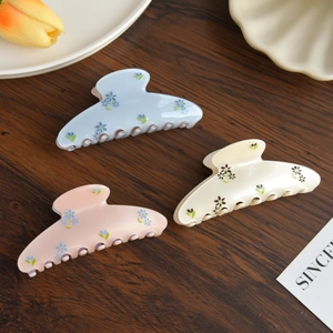 Elegant floral acetate hair claws in blue, pink, and beige displayed on a wooden surface