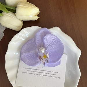 Detailed macro of a purple silk orchid hair clip featuring a large pearl center piece