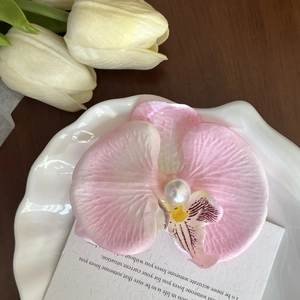 Close-up of a pink orchid hair clip with a white pearl on a decorative plate