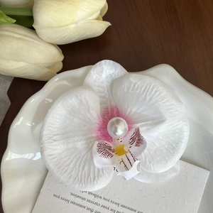 Detailed view of a white silk orchid hair clip with a pearl center on a ceramic plate