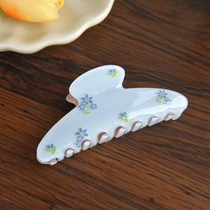 Close-up detail of acetic acid hair claw clip with blue floral pattern on wood background