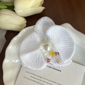 Detail of white orchid hair clip with realistic fabric petals and center pearl