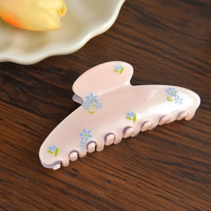 Detail shot of a pink acetate hair claw with delicate blue floral patterns on a wood base