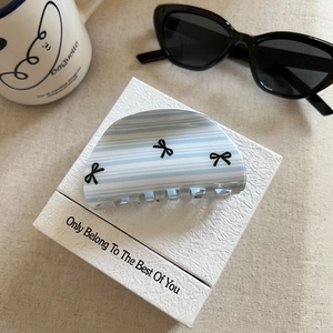 Close-up of blue striped acetate hair claw clip with black bows on a white gift box