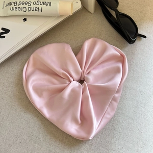 Detailansicht eines rosa Satin-Haargummis in Herzform auf beigefarbenem Strukturstoff