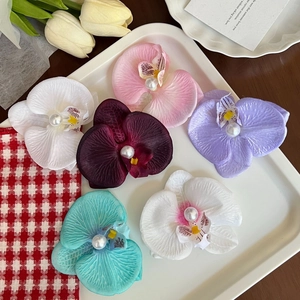Elegant silk orchid hair clips with pearls in various colors on a cream tray