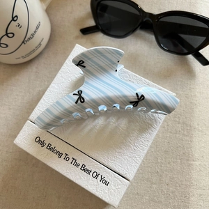 Detail view of large blue striped acetate hair claw clip with bow print on display card