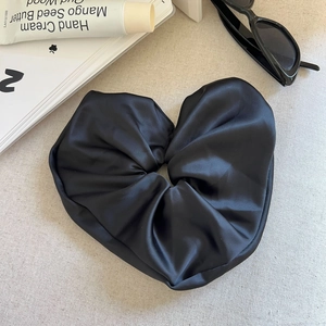 Makroaufnahme von großem schwarzem Herz-Satin-Scrunchie auf stilvollem beigen Hintergrund