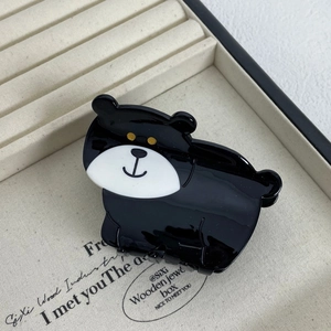 Detail view of a glossy black acetate bear-shaped hair claw clip on a beige tray