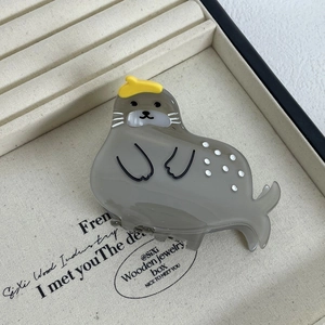 Detail shot of a cute gray acetate seal hair claw clip with a yellow hat on a jewelry tray