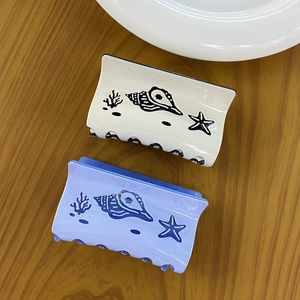 Detailed top view of cream and purple acetate hair claws with delicate sea shell patterns