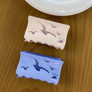 Detail of pink and light blue hair claws with hollowed seagull and sun patterns on wood
