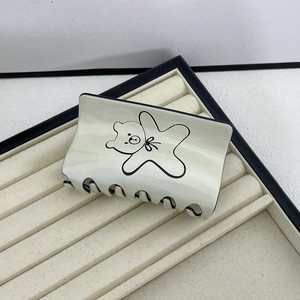 Detail view of cream acetate hair claw clip with black piping and cute bear pattern