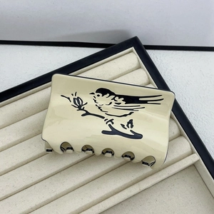 Detail view of cream acetate hair claw clip featuring an elegant black bird on branch design